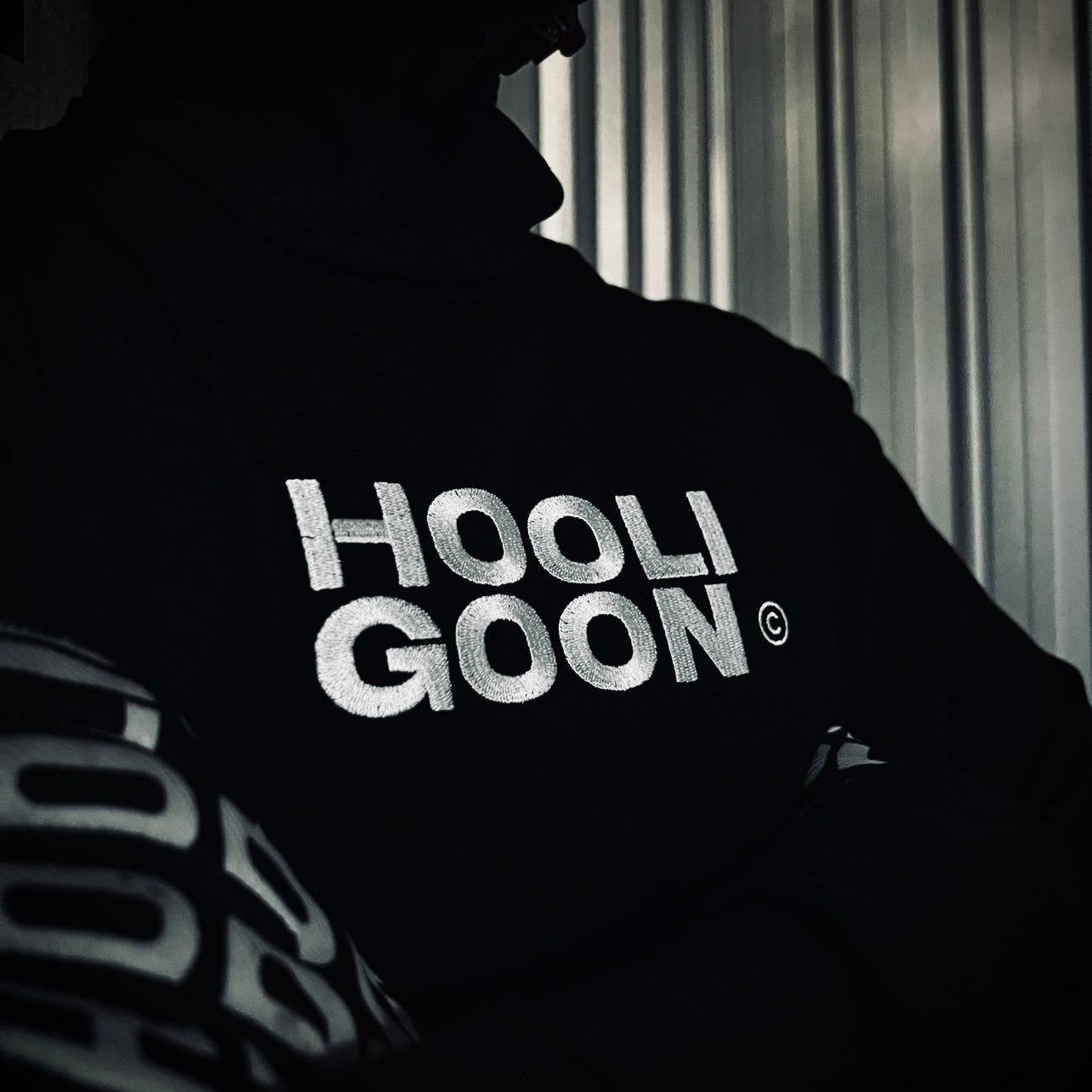 Person wearing a hoodie with 'HOOLIGOON' text in a dark setting