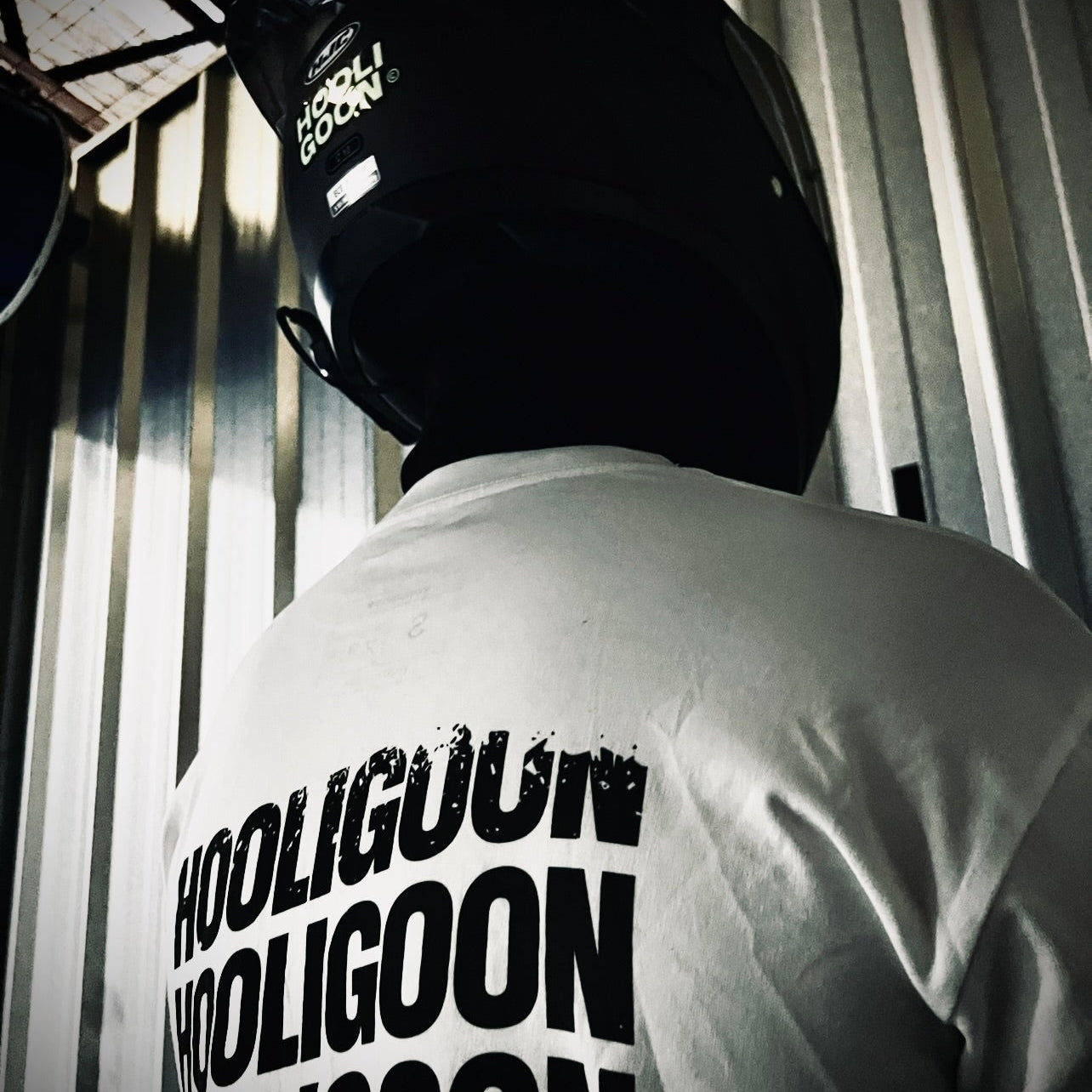 Person wearing a white t-shirt with 'HOOLIGOON' text, standing in a dimly lit room.