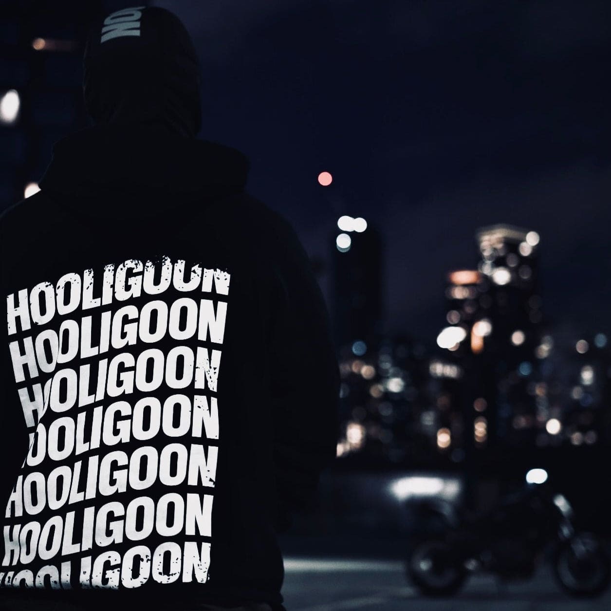 Person wearing a hoodie with 'Hooligoon' text at night in an urban setting.