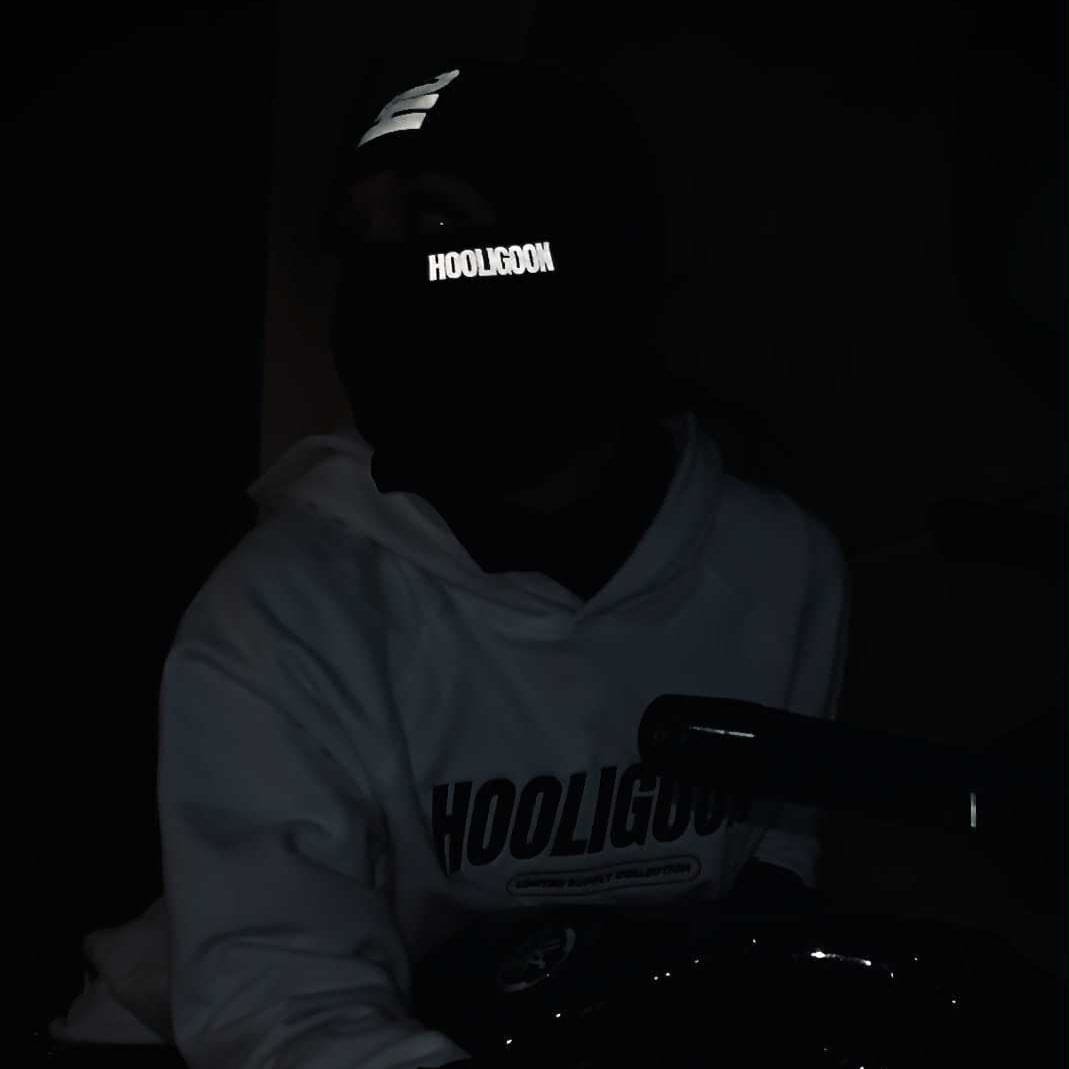 Person wearing a reflective 'Hooligoon' mask at night with city lights in the background