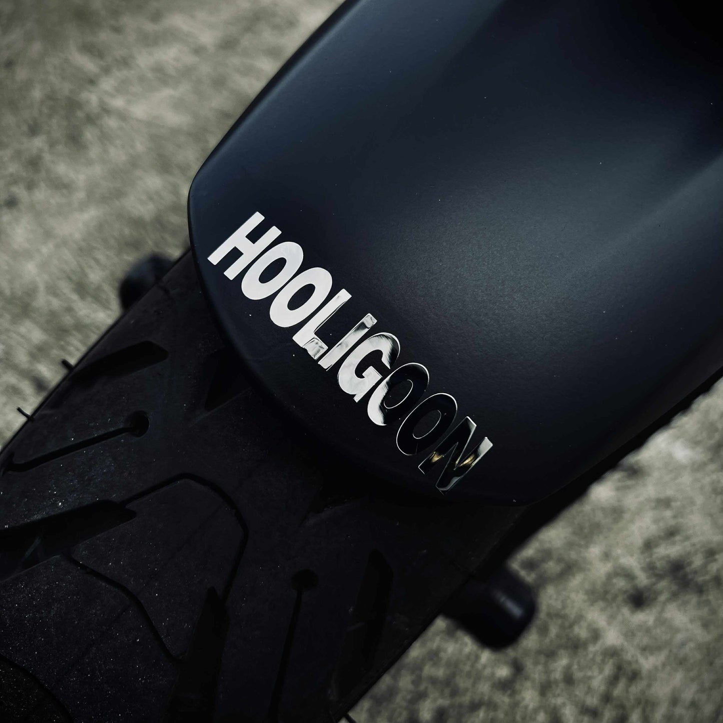 Close-up of a black motorcycle fender with 'HOOLIGOON' branding on a textured surface.