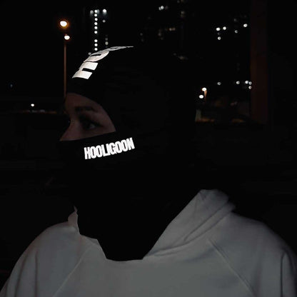Person wearing a reflective 'Hooligoon' mask at night with city lights in the background