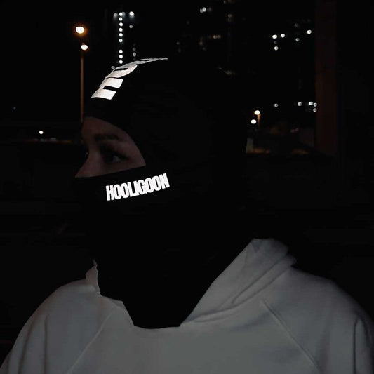 Person wearing a reflective 'Hooligoon' mask at night with city lights in the background