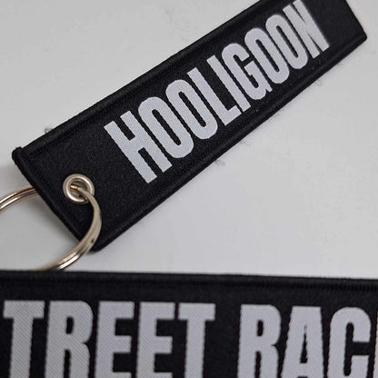 Two black key tags with white text, one reading 'STREET RACER' and the other 'HOOLIGOON'. They are laid out on a white surface.