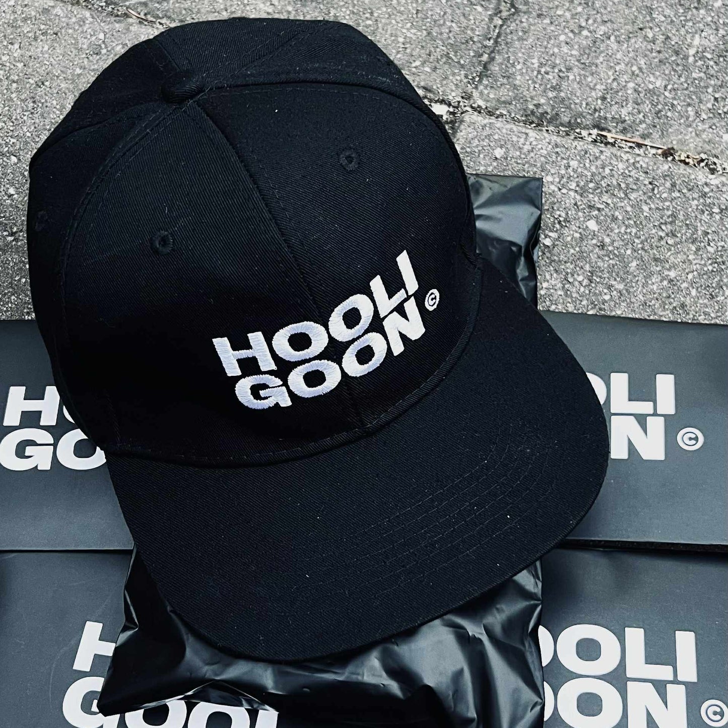 Black cap with 'HOOLIGOON' branding on a branded surface
