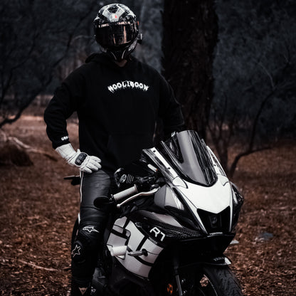 Person on a motorcycle in a forest setting wearing a black hoodie with visible branding.