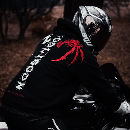 Person wearing a black hoodie with red and white designs, sitting on a motorcycle in a dark setting.