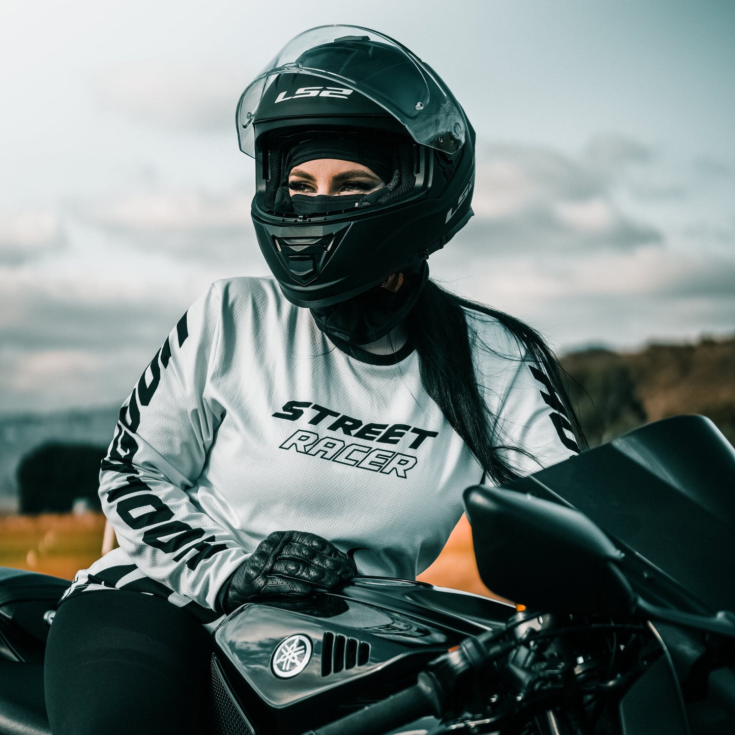 Person wearing a helmet and 'Street Racer' shirt sitting on a motorcycle with a blurred background.