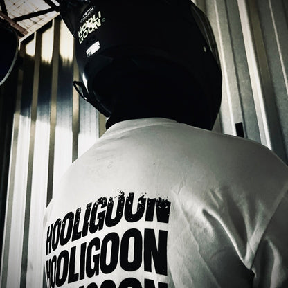 Person wearing a white t-shirt with 'HOOLIGOON' text, standing in a dimly lit room.