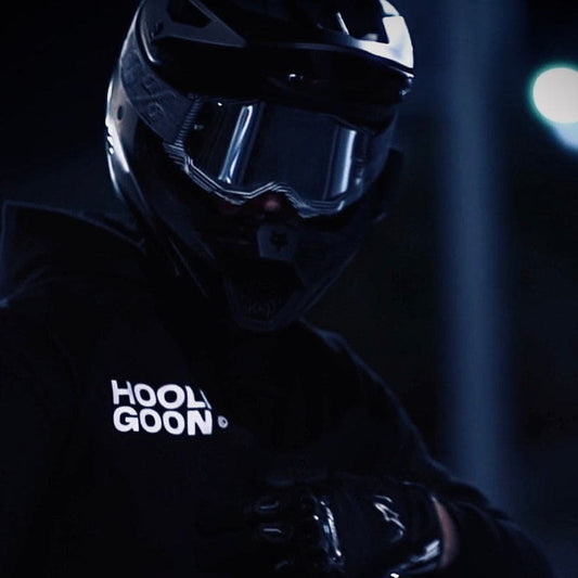 Person wearing a black motorcycle helmet and jacket with 'Hooligoon' branding in a dark setting.
