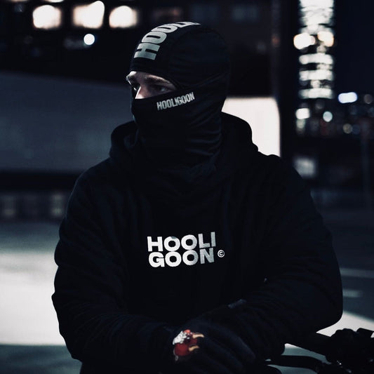 Person wearing a dark hoodie with 'HOOLIGOON' text, sitting against a blurred cityscape background.