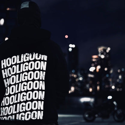 Person wearing a hoodie with 'Hooligoon' text at night in an urban setting.