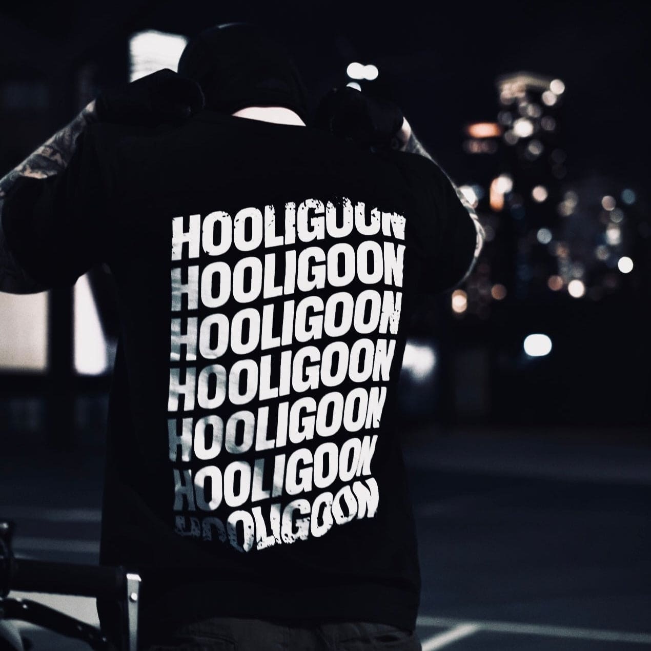 Person wearing a black tee with 'HOOLIGOON' text in white, standing in a dark setting.