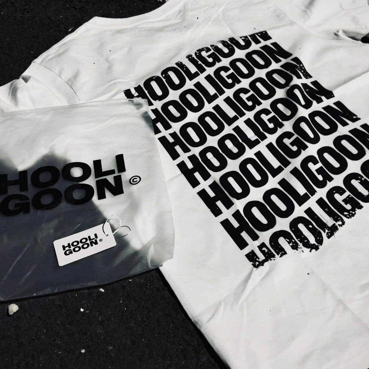 White t-shirt with 'HOOLIGOON' text and packaging on a dark surface