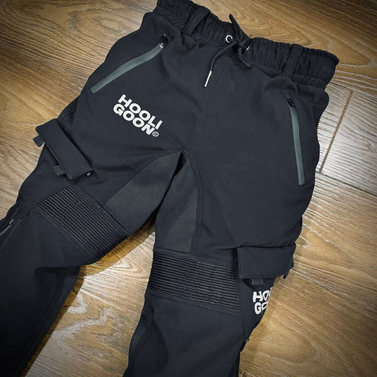 Black snow pants with 'Hooligoon' branding on a wooden floor