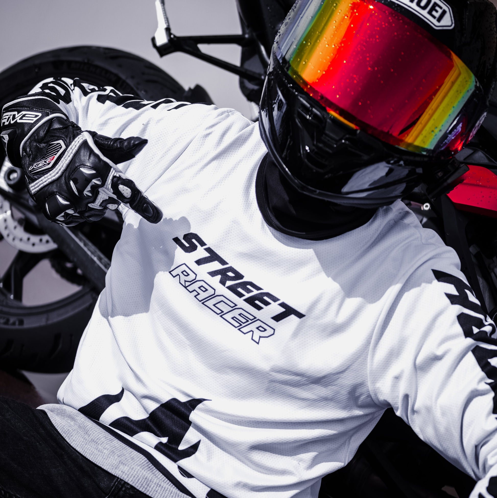 Person wearing a white 'Street Racer' t-shirt and colorful helmet sitting on a motorcycle.